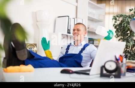 Relaxed cleaning service worker sitting in office with feet on table Stock Photo