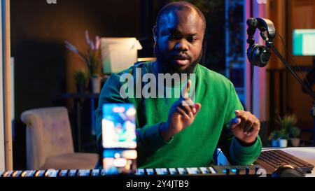 Musician doing online paid classes to help people play piano notes, teaching lessons from his home studio and recording video tutorials. Musical instructor playing midi controller keyboard. Camera A. Stock Photo
