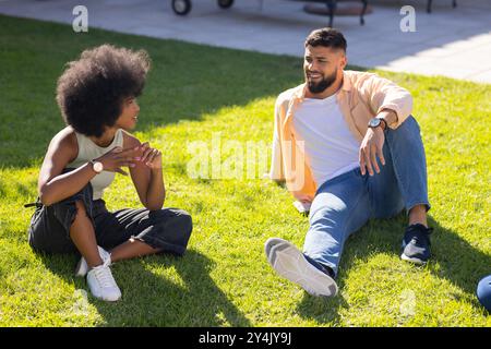 Sitting on grass, young diverse friends talking and enjoying outdoor time together Stock Photo
