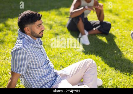 Relaxing on grass, young man enjoying outdoor time with diverse friends Stock Photo