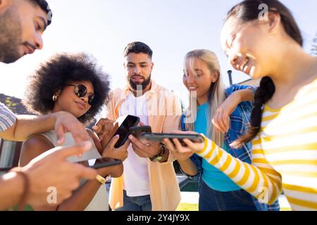 Group of young diverse friends using smartphones and tablets, enjoying outdoor time together Stock Photo