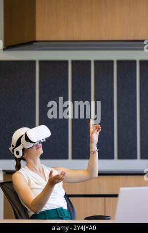 Using VR headset, woman in office interacting with virtual environment, copy space Stock Photo