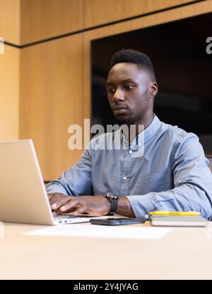 Working on laptop, man focusing on business tasks in modern office setting Stock Photo