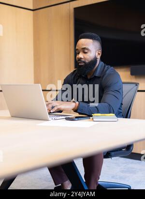 Working on laptop, man sitting at desk in modern office setting Stock Photo