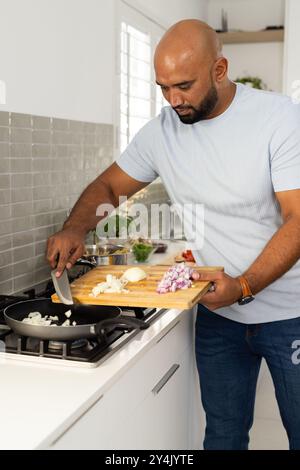 Cooking in kitchen, man adding chopped onions from cutting board to frying pan Stock Photo