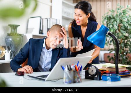 Upset office employe looking on laptop with disgruntled female manager Stock Photo