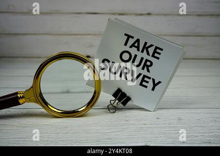 Take Our Survey text message on sticky note with magnifying glass on wooden background Stock Photo
