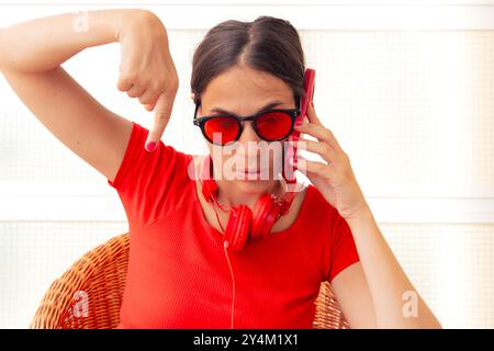 A young woman in sunglasses is sitting, pointing her finger down Stock Photo