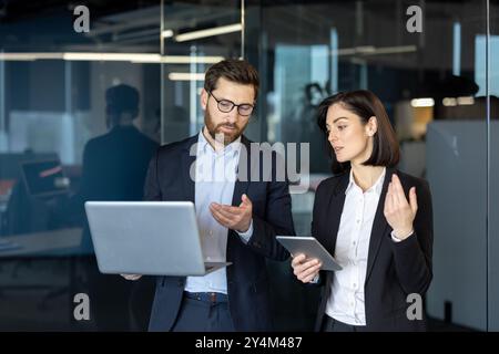Colleagues engaged in professional business meeting, discussing work on laptop and tablet. Teamwork and collaboration evident in modern office setting, conveying productivity and corporate strategy. Stock Photo