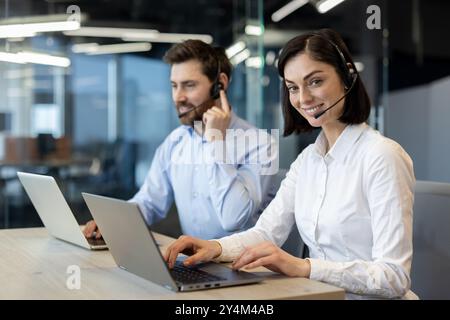 Customer service representatives working together using laptops and headsets in office. Team collaboration focused on providing excellent service, communicating effectively Stock Photo
