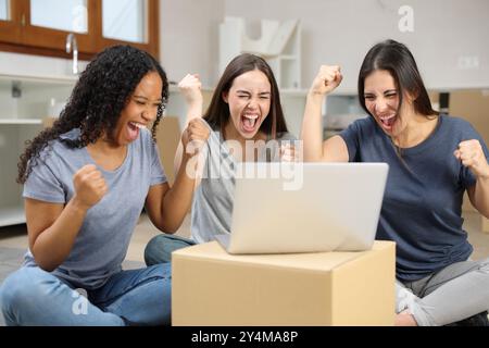 Three excited roommates celebrating success checking laptop moving home Stock Photo
