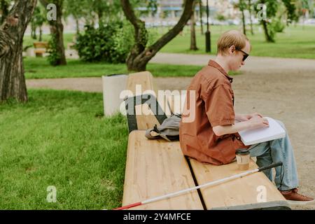 Unrecognizable man sitting on wooden bench and enjoying Braille book in park Stock Photo