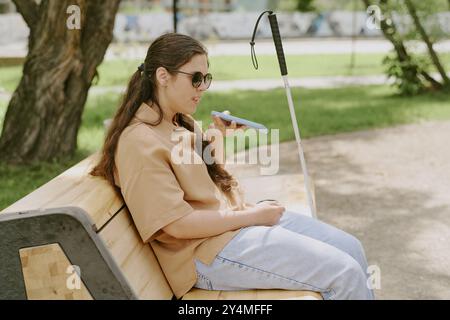 Side view shot of young woman recording voice message in social network while resting on bench in park Stock Photo