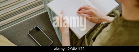 Website banner of Braille book on unrecognizable male knees, man sitting on gray sofa Stock Photo
