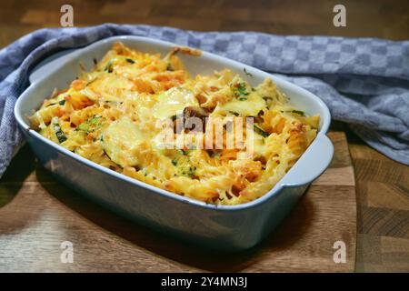 Pasta gratin with vegetables, tomato sauce and cheese in a casserole fresh from the oven on a dark rustic wooden board with a gray kitchen towel, sele Stock Photo