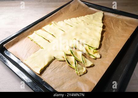 Puff pastry dough filled with homemade green pesto is cut in a Christmas tree on a baking tray, creative recipe for a holiday party, copy space, selec Stock Photo