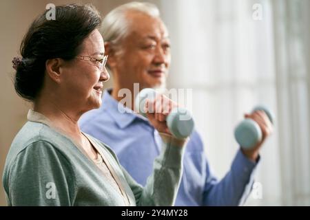 happy senior asian couple exercising at home using dumbbells Stock Photo