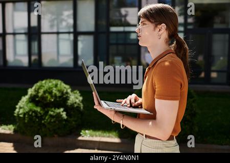 Focused on their laptop, a young non binary individual enjoys working in an open office space. Stock Photo