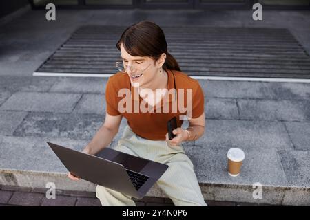 This young non binary individual is focused on their laptop while enjoying coffee in the office. Stock Photo