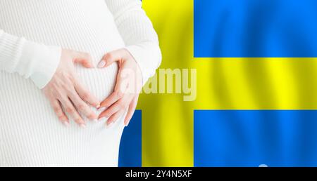 Demographics, pregnancy and love baby in Sweden concept. Pregnant woman making heart against her stomach on Swedish flag background. Stock Photo