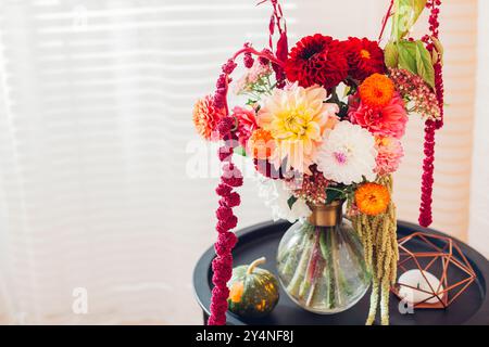 Close up of autumnal bouquet of dahlia flowers with amaranth in vase on table. Fall decor with pumpkin at home. Space Stock Photo