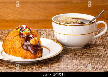 Croissant garnished with chocolate and rainbow sprinkles. French croissant garnished with chocolate and rainbow sprinkles in brown ceramic dish with a Stock Photo
