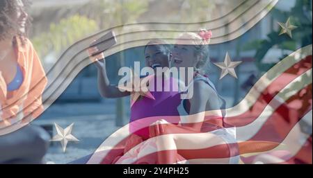 Image of american flag elements over happy diverse female friends taking selfies on sunny beach Stock Photo