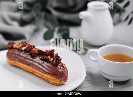 Eclair with Chocolate Cream and Hazelnuts and tea Stock Photo