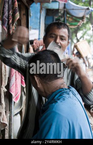 Mumbai, Maharashtra / India - June 7, 2008: A barber cutting hairs of a man on the street. Stock Photo