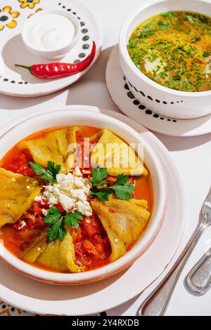 Vibrant bowl of spicy soup served with stuffed peppers, garnished with fresh herbs and cheese Stock Photo