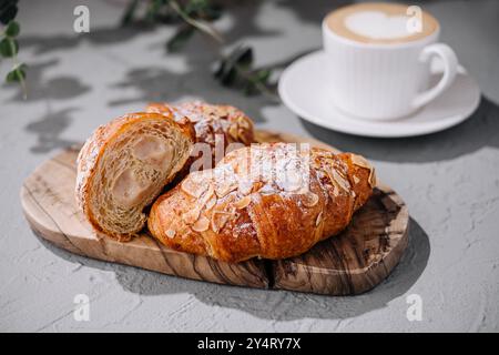 Fresh almond croissants on a wooden board with latte art coffee in the background Stock Photo