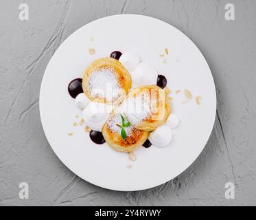 Elegant serving of pancakes topped with powdered sugar, cream, and berry sauce on a white plate Stock Photo