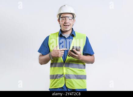 Smiling engineer holding phone and looking at camera isolated. Latin male builder engineer using phone isolated Stock Photo