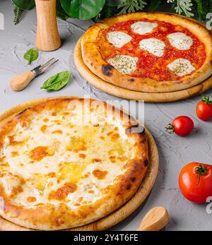 Freshly baked margherita and four cheese pizzas served on wooden boards, garnished with tomatoes and basil Stock Photo