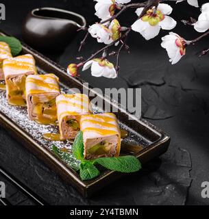 Elegant sushi rolls with kiwi and banana served on a platter with a sakura branch, on a dark stone background Stock Photo