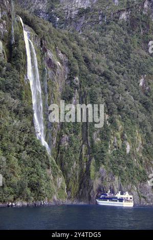 Milford Sound, New Zealand, circa 2009: A tourist Launch at a waterfall, Milford Sound, Fiordland, New Zealand, Oceania Stock Photo