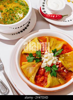 Vibrant bowl of spicy soup served with stuffed peppers, garnished with fresh herbs and cheese Stock Photo