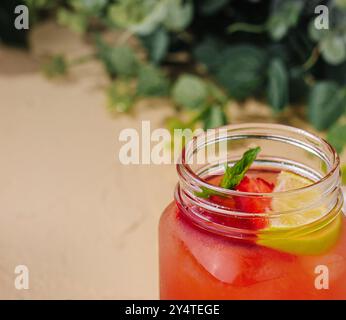 Iced strawberry lemonade garnished with fresh mint and lemon in a mason jar on a sandy background Stock Photo