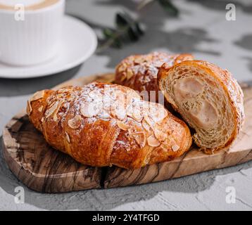 Fresh almond croissants on a wooden board with latte art coffee in the background Stock Photo