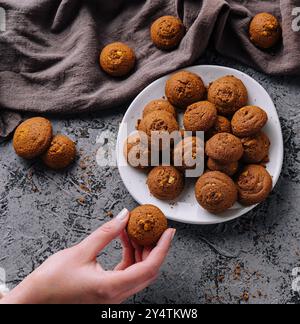 A person's hand reaching for delicious oatmeal cookies arranged on a plate, with a rustic vibe Stock Photo