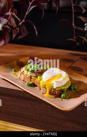 Two slices of whole grain bread with mashed avocado and poached eggs decorated with pea seeds and spices Stock Photo