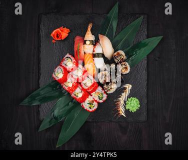 Different types of sushi are lying on green leaves on a black stone plate Stock Photo