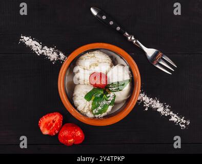 Three balls of ice cream lying in a bowl and decorated with mint and strawberry on a black wooden table Stock Photo