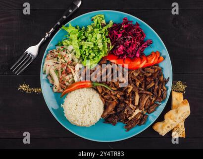 Traditional turkish iskender kebab with rice, vegetables and pita bread on a blue plate, lying on a dark wooden table Stock Photo