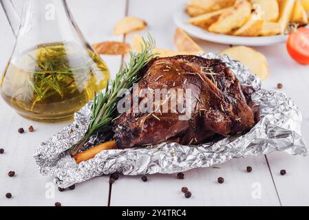 Delicious roasted lamb leg seasoned with rosemary and spices, served on a white wooden table with roasted potato wedges Stock Photo