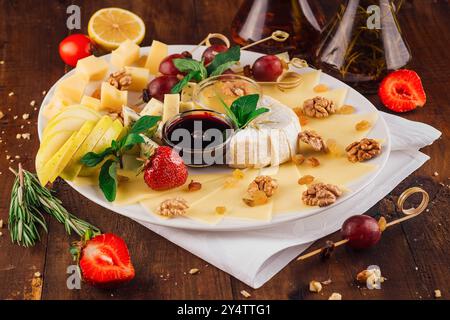 Cheese plate presenting variety of cheeses with fruits and nuts on wooden table Stock Photo