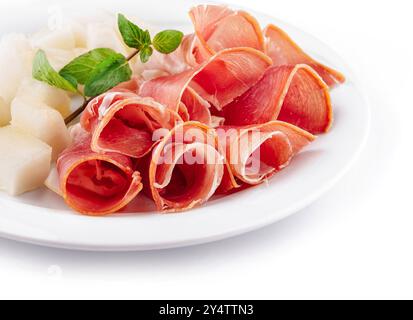 Slices of prosciutto with cantaloupe melon on a white plate garnishing with fresh mint Stock Photo