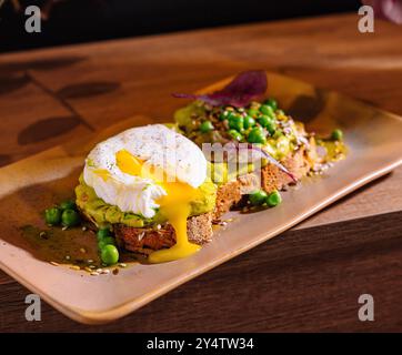 Two slices of whole grain bread with mashed avocado and poached eggs decorated with pea seeds and spices Stock Photo