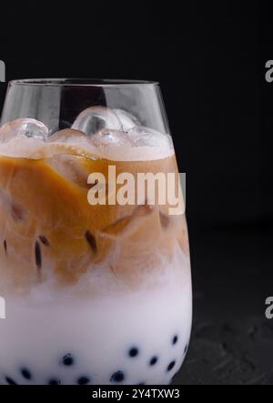 Glass filled with refreshing iced coffee mixed with milk and boba balls over black background Stock Photo