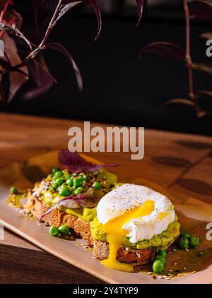 Two slices of whole grain bread with mashed avocado and poached eggs decorated with pea seeds and spices Stock Photo